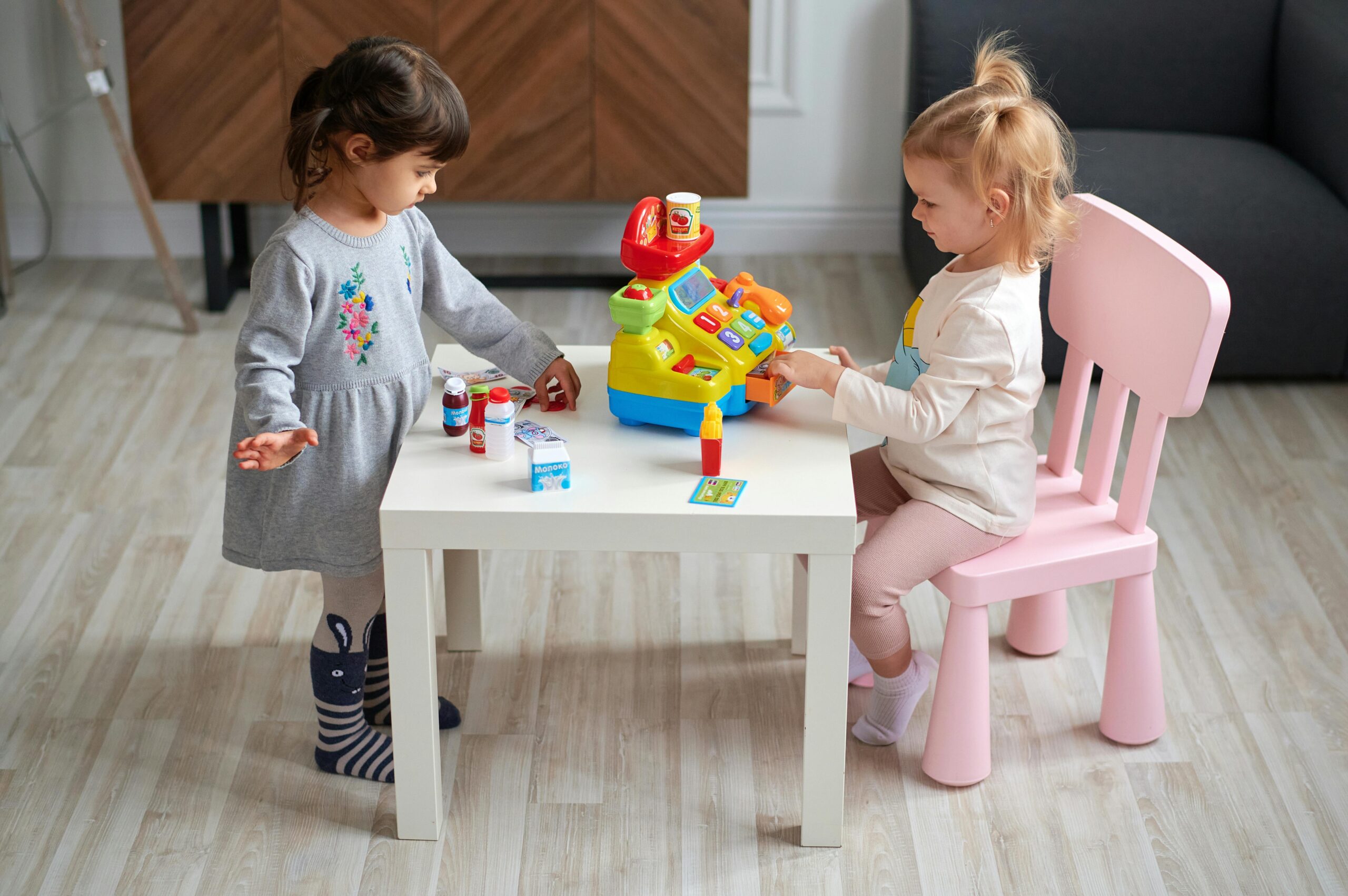 Two young girls engaged in imaginative play with a toy cash register at home.