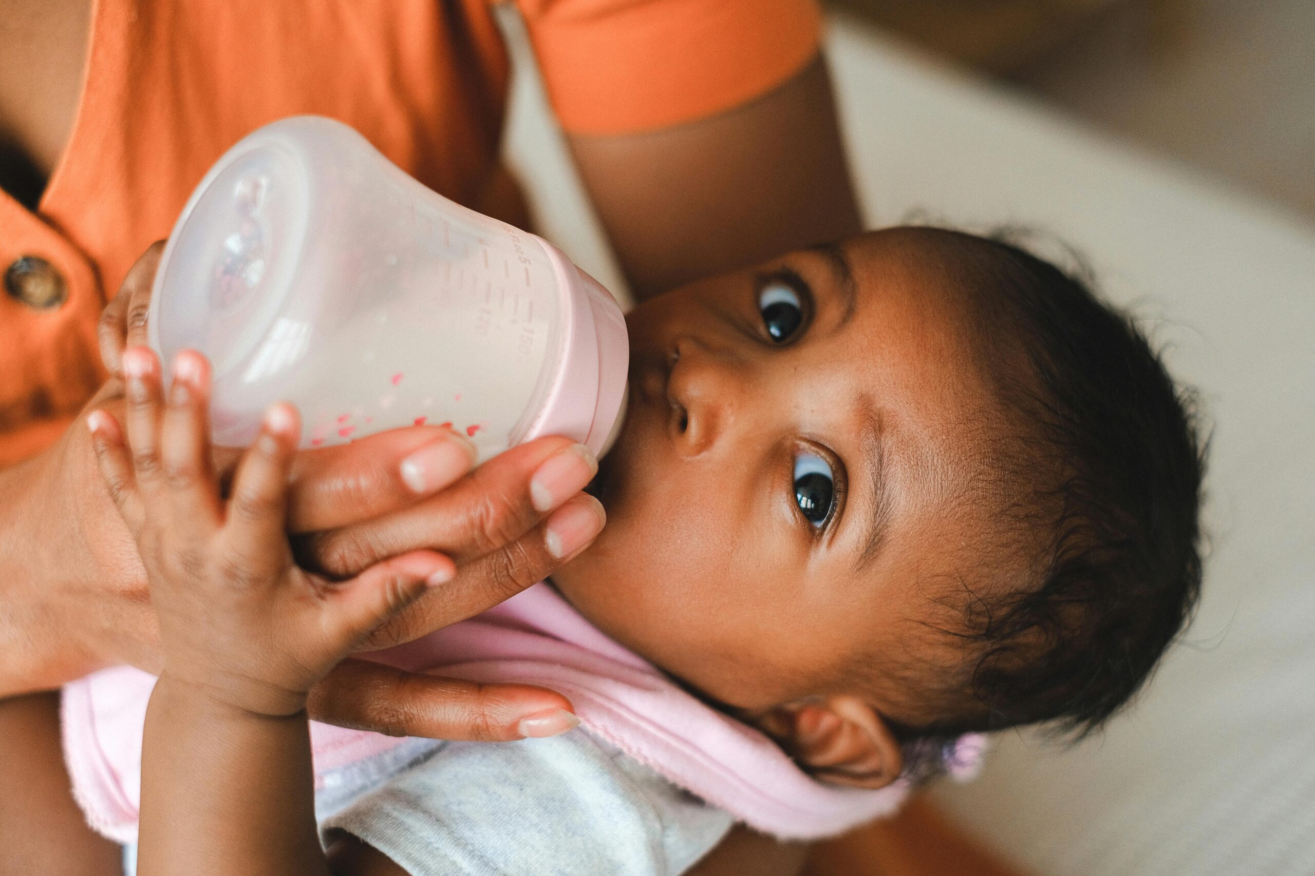 Close-up of a mother feeding her baby with a milk bottle indoors.