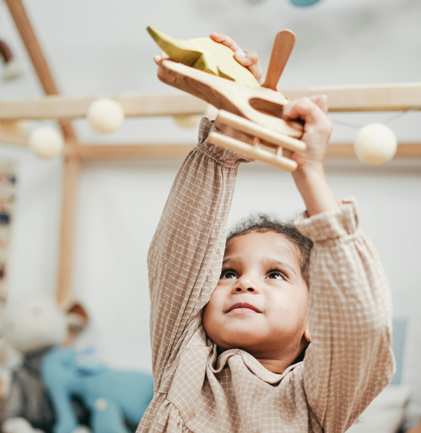 Happy child playing with wooden airplane indoors, exuding joy and innocence.