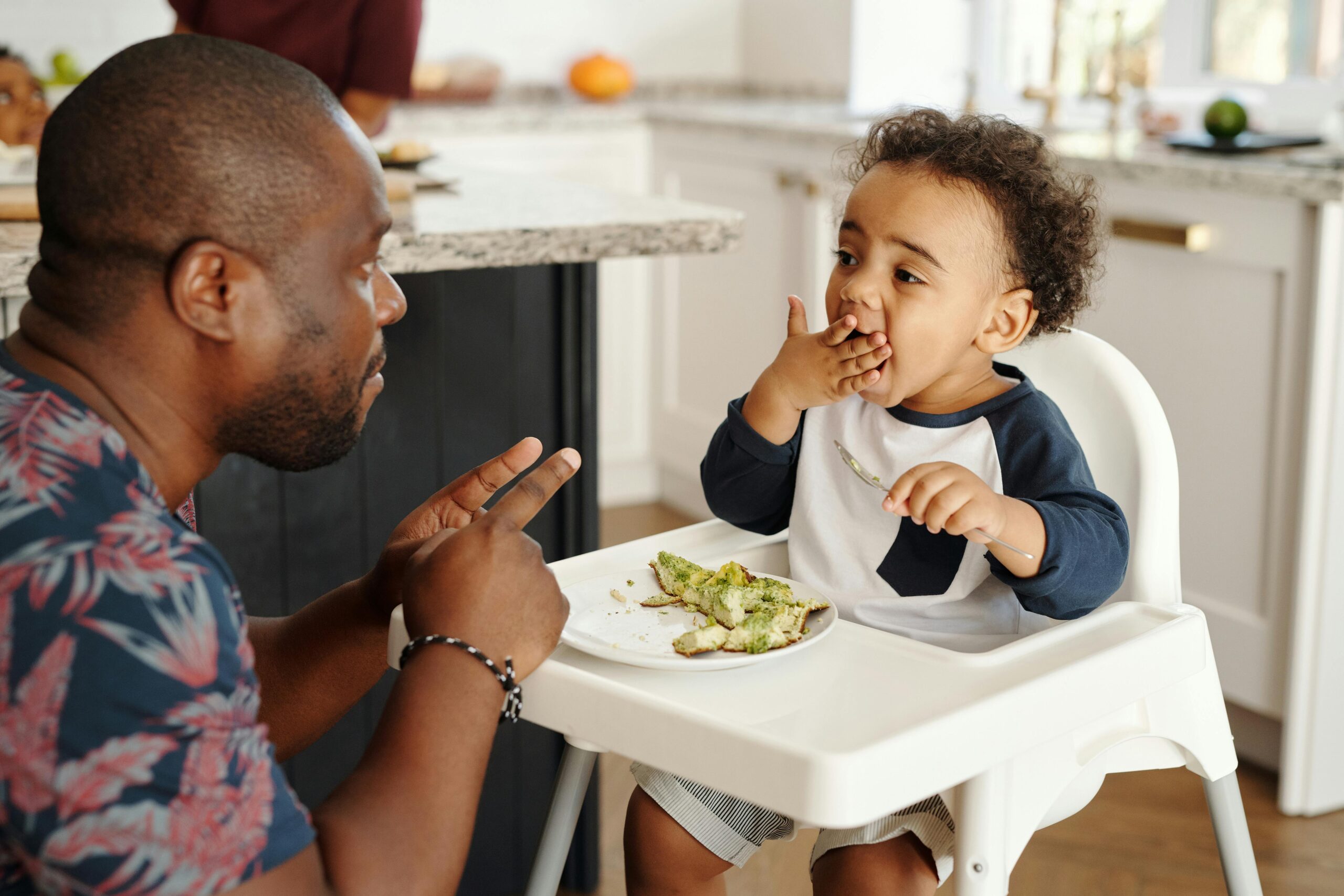 A father and his young son share a playful breakfast moment in the kitchen.